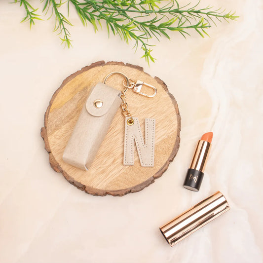 Beige personalised keychain pouch on a wooden coaster beside a lipstick