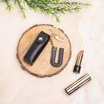 Black personalised keychain pouch on a wooden coaster beside a lipstick