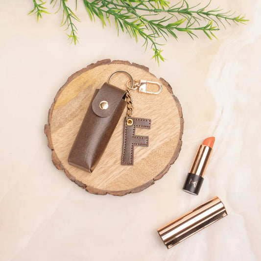 Brown personalised keychain pouch on a wooden coaster beside a lipstick