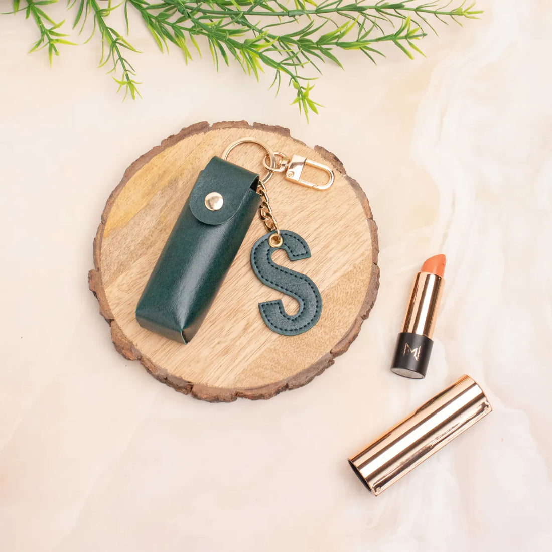 Green personalised keychain pouch on a wooden coaster beside a lipstick
