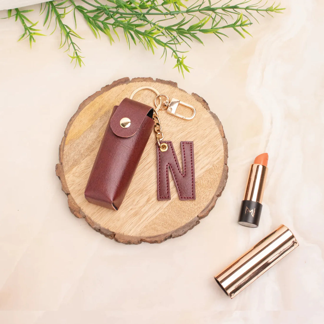 Maroon personalised keychain pouch on a wooden coaster beside a lipstick