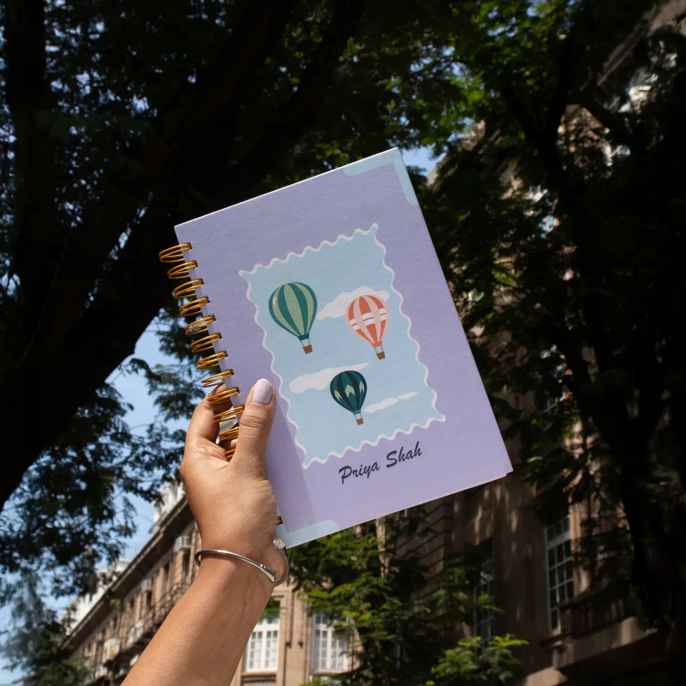 Hand holding hot air balloon notebook with name 'Priya Shah'